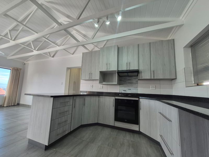 Modern kitchen featuring light wood-grain cabinetry, dark granite countertops, built-in oven, extractor fan, and an impressive exposed truss ceiling with tiled flooring.