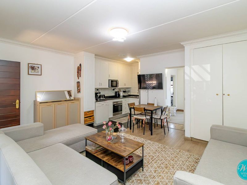 Open-plan living area featuring a functional kitchen with built-in cabinetry, integrated appliances, and laminate flooring, seamlessly connecting to the lounge space.