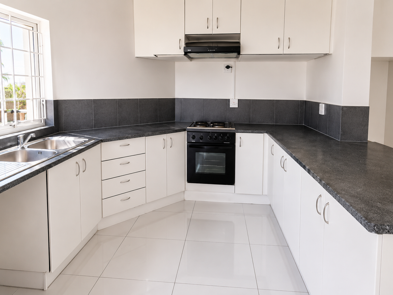 A clean, modern kitchen featuring white cabinetry, dark laminate countertops, a built-in oven with hob, and tiled flooring.