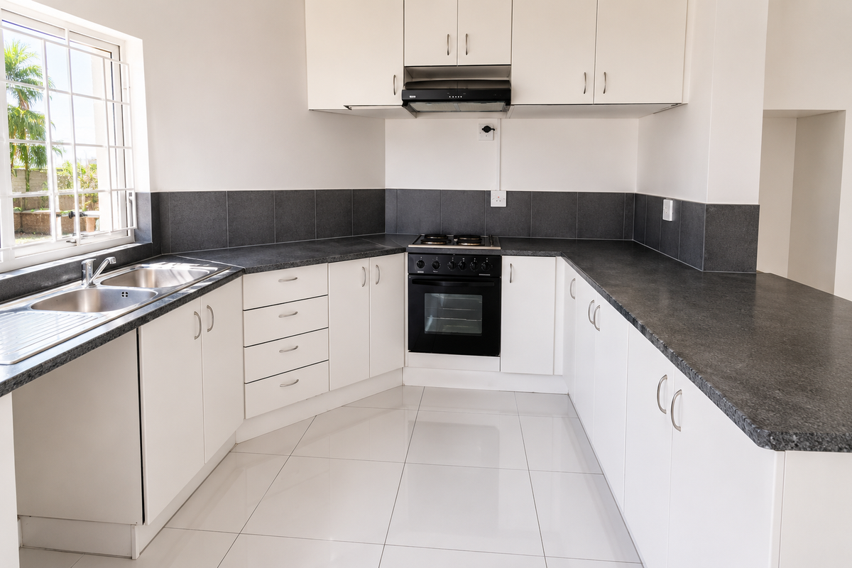 A clean, modern kitchen featuring white cabinetry, dark laminate countertops, a built-in oven with hob, and tiled flooring.