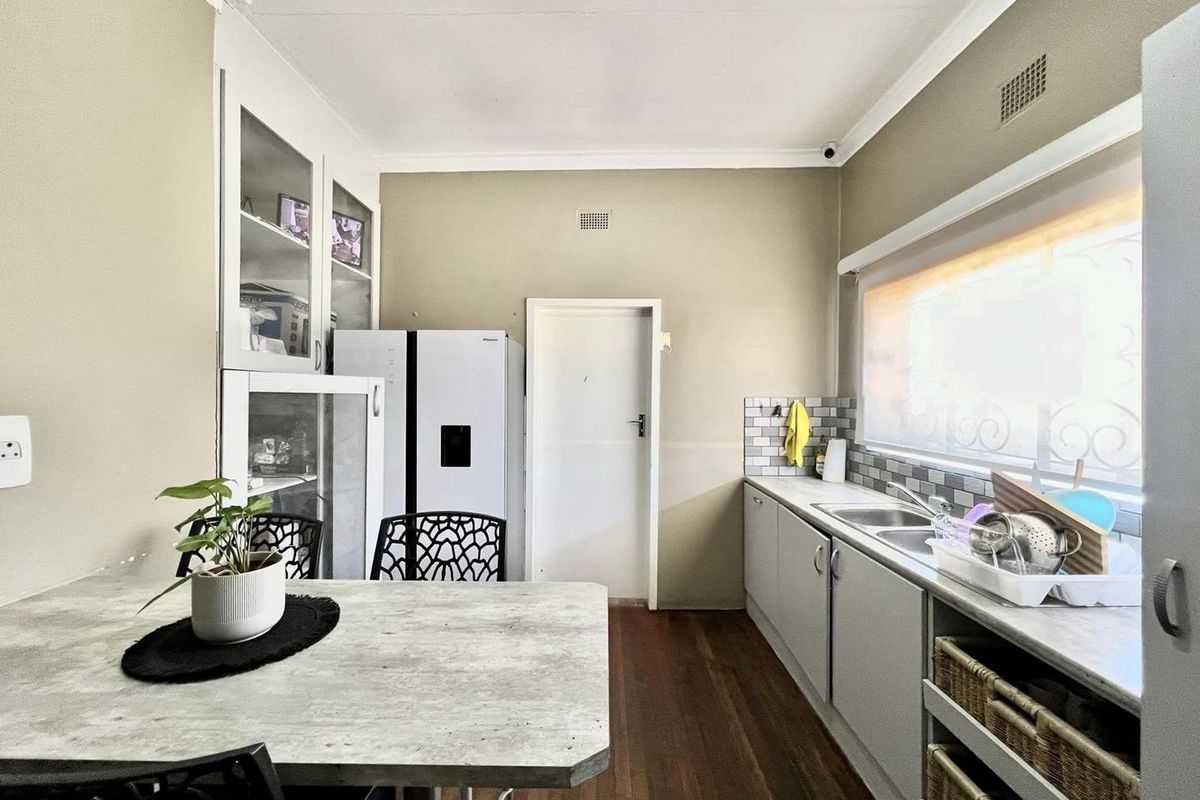 A functional kitchen area featuring built-in cabinetry, a stainless steel sink, tiled backsplash, and integrated storage solutions with wood-look flooring.