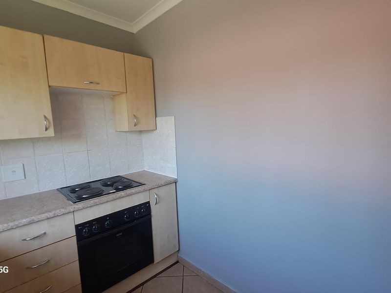 A compact kitchen featuring light wood-finish cabinetry, a built-in oven with electric hob, and tiled splashback, offering a functional layout.