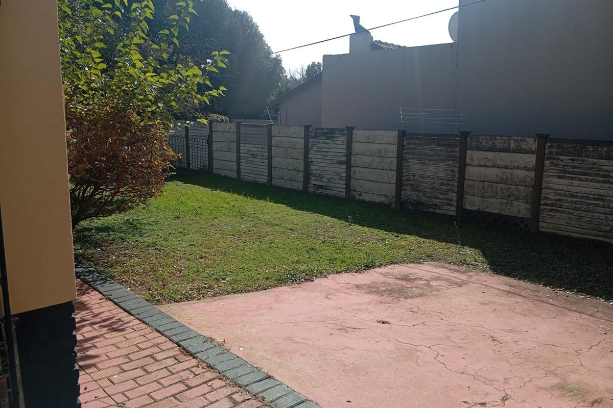 A rear garden area featuring a paved patio, a small lawn, and a precast concrete boundary wall.