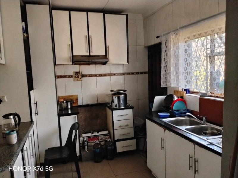 A functional kitchen featuring built-in cabinetry, a double basin sink, and tiled splashbacks, offering a practical layout ready for modernization.