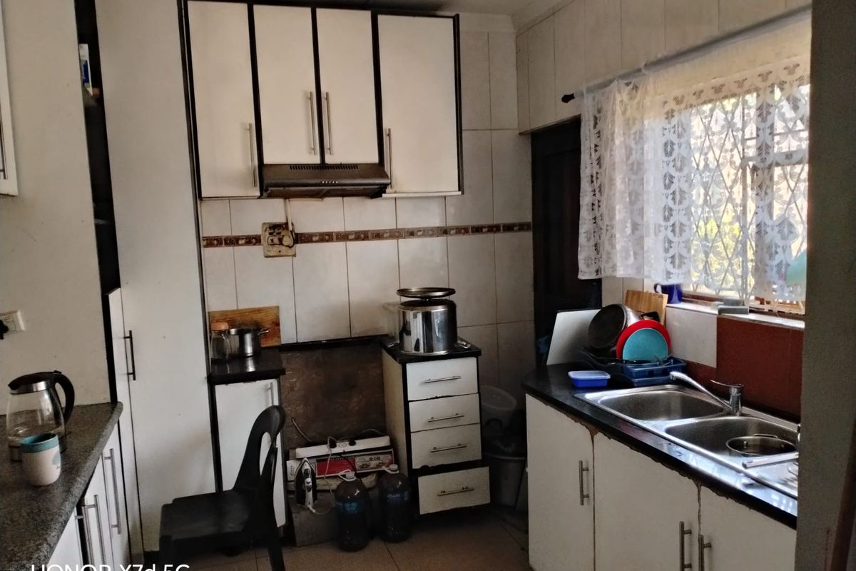 A functional kitchen featuring built-in cabinetry, a double basin sink, and tiled splashbacks, offering a practical layout ready for modernization.