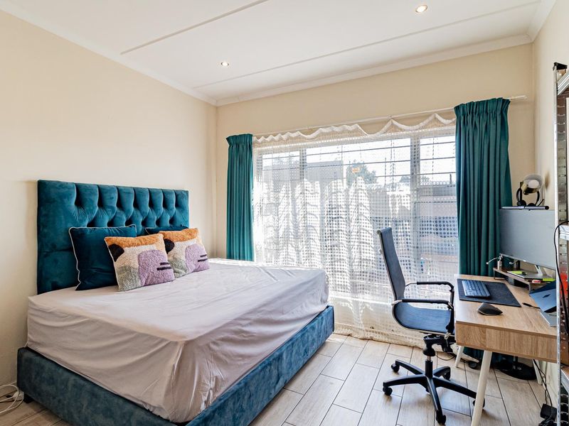 A well-lit bedroom featuring tiled flooring, recessed ceiling lighting, and a large window fitted with security bars.
