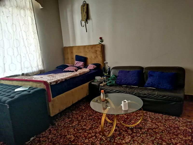 A bedroom space featuring a bed and seating area, showing signs of wear on the walls and requiring cosmetic updates.