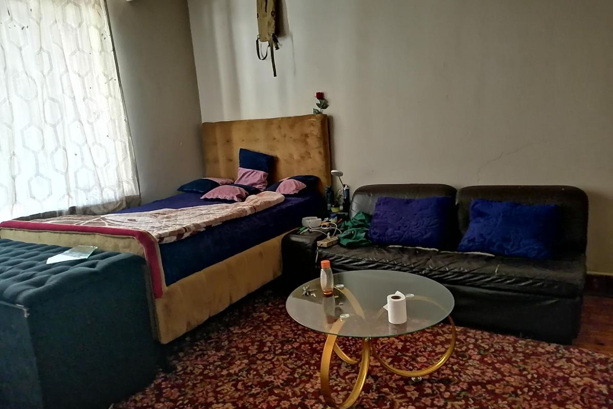 A bedroom space featuring a bed and seating area, showing signs of wear on the walls and requiring cosmetic updates.
