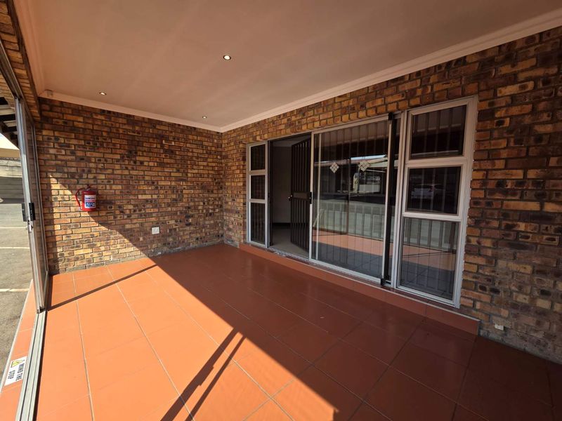 A covered patio area featuring exposed brick walls, tiled flooring, and sliding glass doors providing access to the office interior.