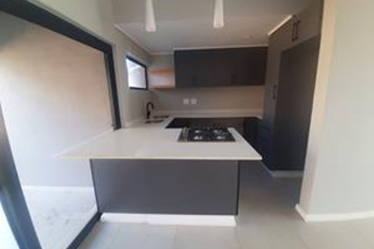 Modern kitchen featuring dark cabinetry, stone countertops, integrated gas hob, and large sliding glass doors providing seamless access to the outdoor area.