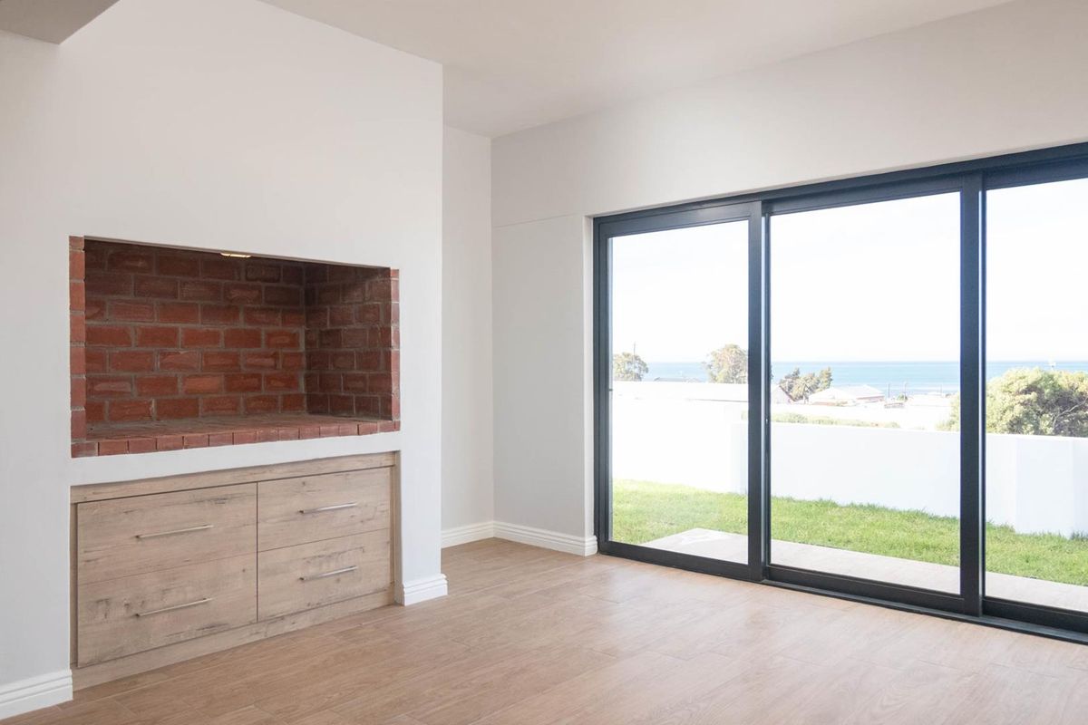 A bright living area featuring a built-in brick fireplace, modern cabinetry, and large sliding glass doors opening to a garden with ocean views.