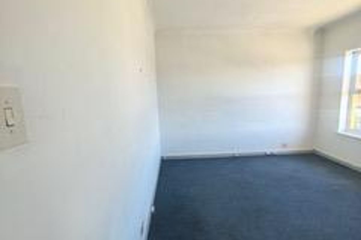 An empty, carpeted office space featuring neutral walls and a standard fluorescent light fixture, suitable for a professional workspace.