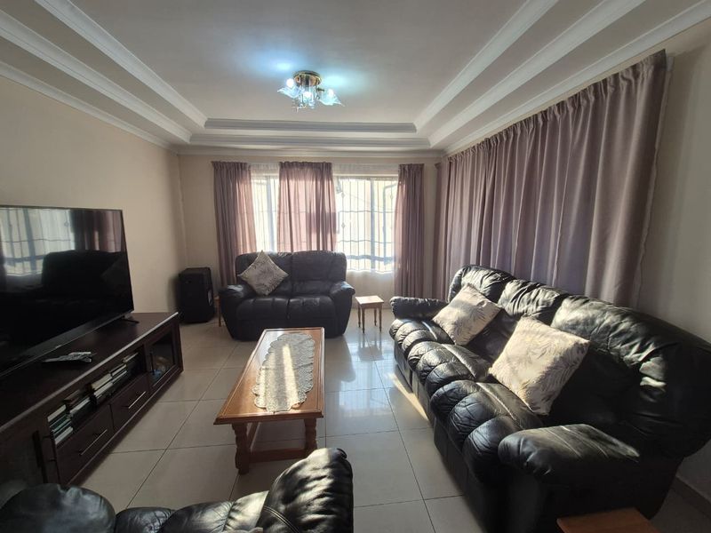 A comfortable living room featuring tiled flooring, a tray ceiling with decorative molding, and large windows fitted with security bars.