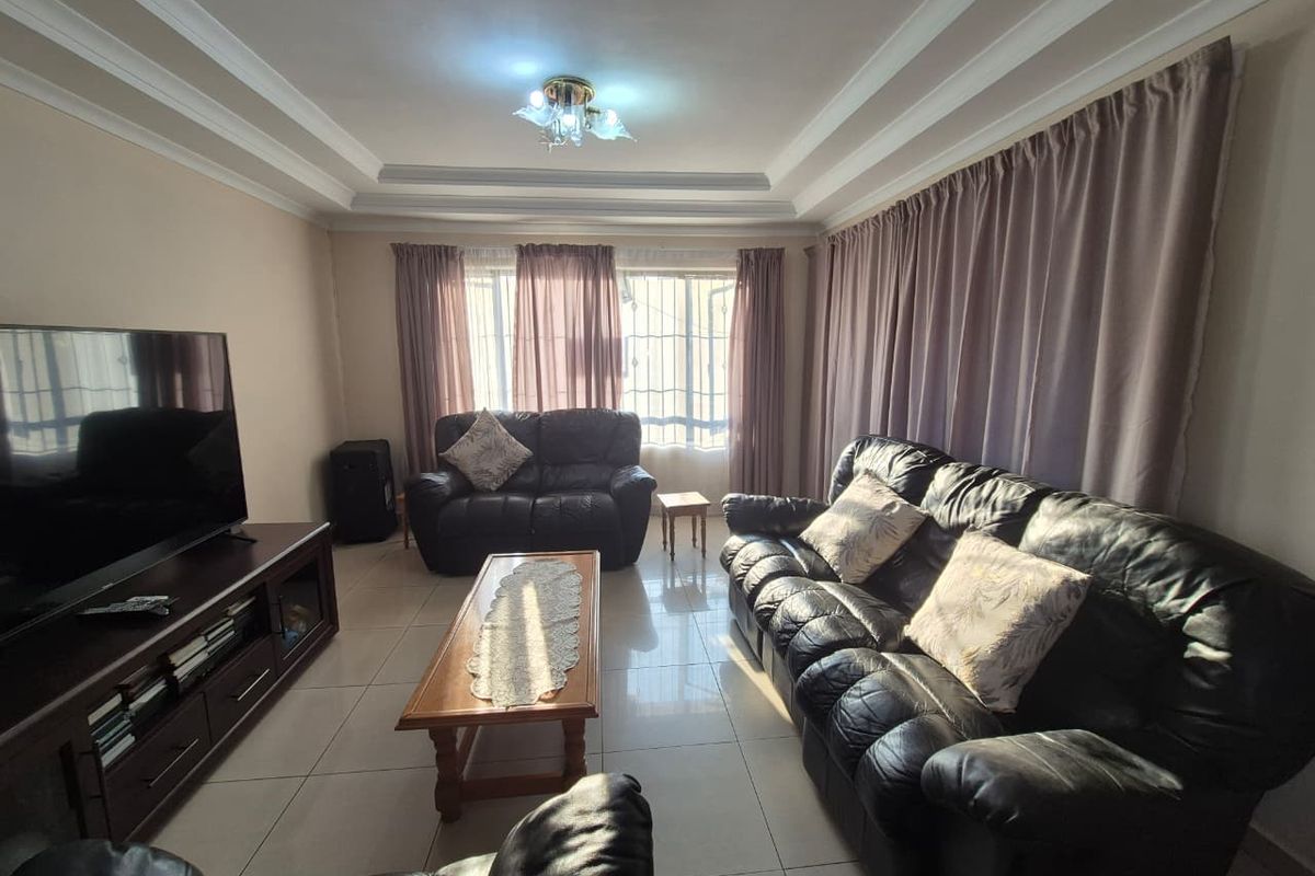 A comfortable living room featuring tiled flooring, a tray ceiling with decorative molding, and large windows fitted with security bars.