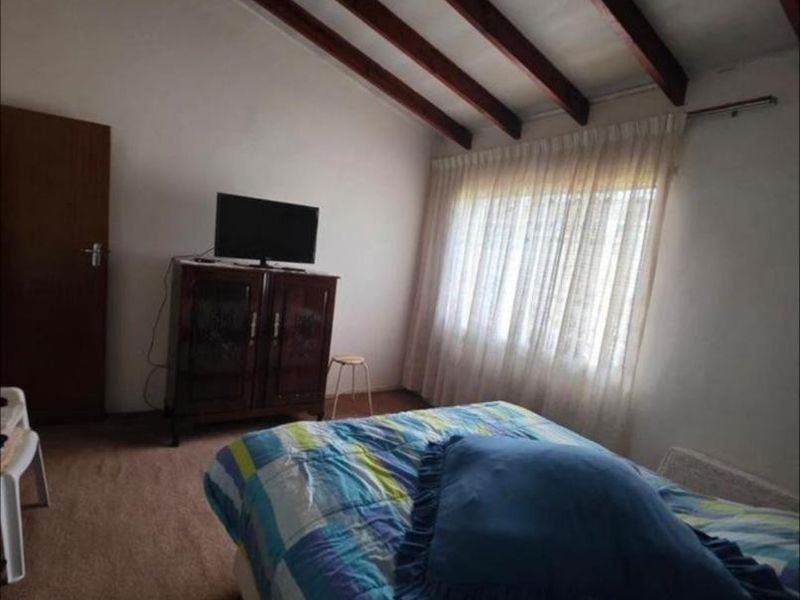 A bedroom featuring a vaulted ceiling with exposed timber beams and large windows with curtains.