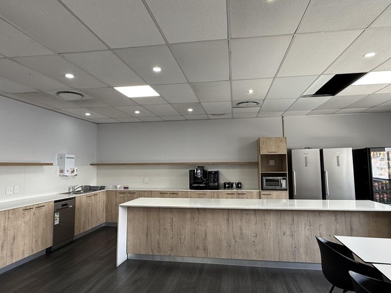 Modern office kitchen area featuring light wood cabinetry, stone countertops, integrated appliances, and a functional island workspace under a suspended ceiling.