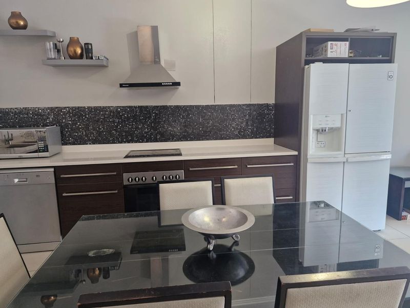 Open plan kitchen featuring dark wood cabinetry, mosaic tile backsplash, stone countertops, and integrated stainless steel appliances.