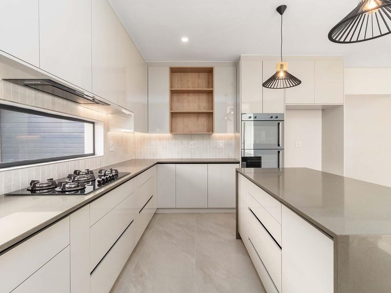 Modern kitchen featuring sleek cabinetry, stone countertops, a gas cooktop, built-in oven, and a central island with integrated lighting.