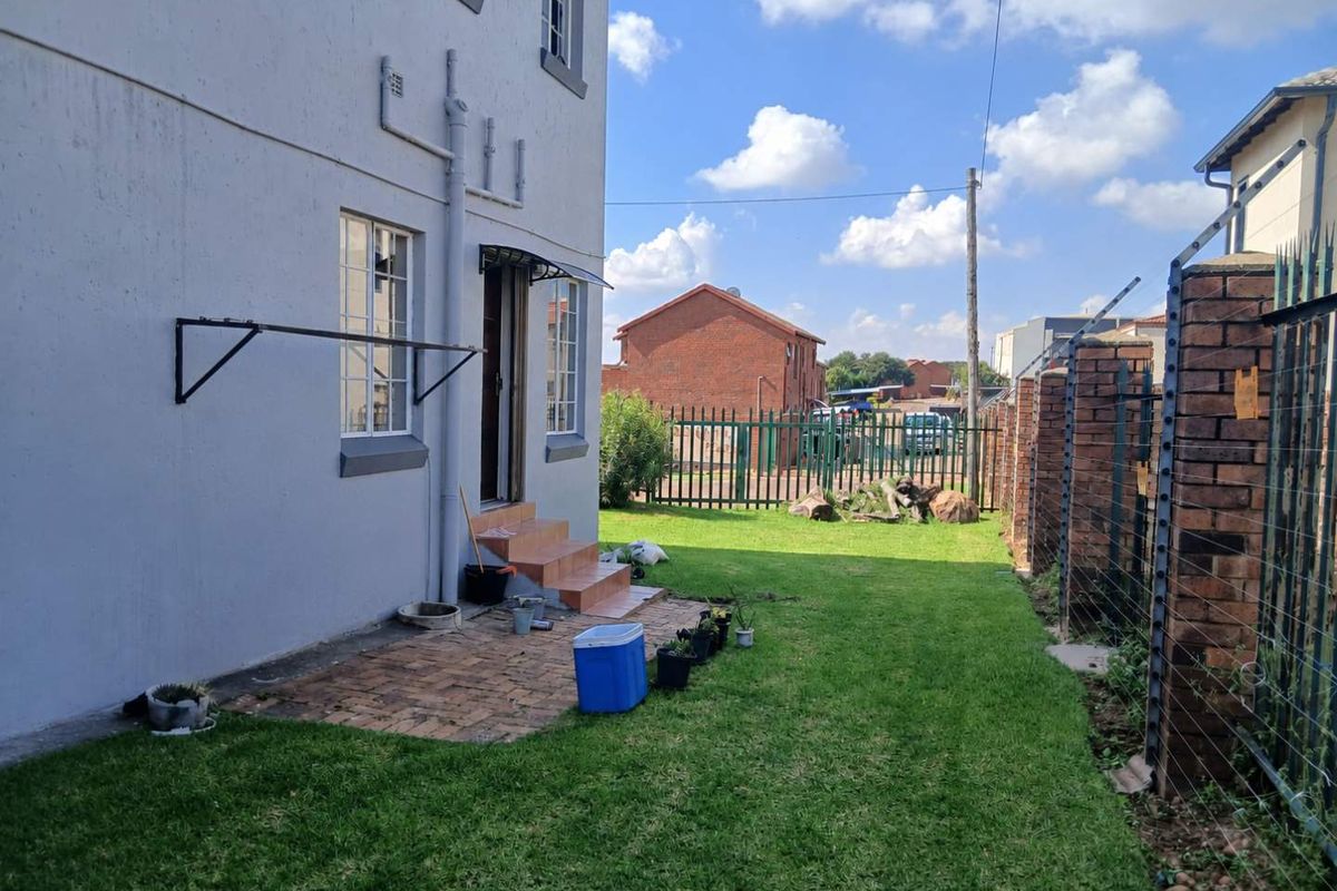 Rear exterior view of the property featuring a small paved patio, tiled entrance steps, and a fenced garden area with electric security fencing.
