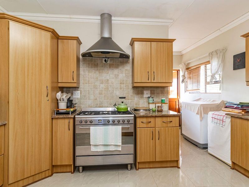 A functional kitchen featuring wooden cabinetry, granite countertops, a stainless steel gas stove with extractor fan, and tiled flooring.