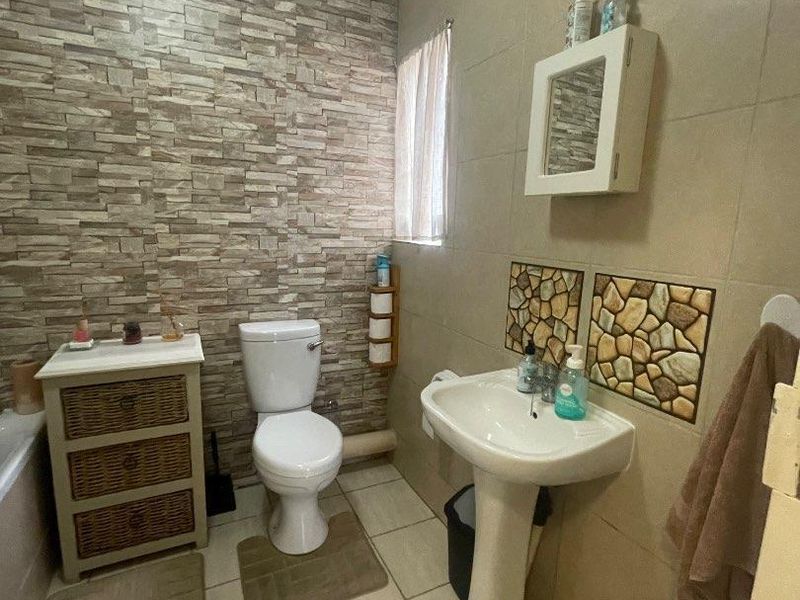 A functional bathroom featuring a pedestal basin, toilet, tiled flooring, and a decorative stone-cladding feature wall.