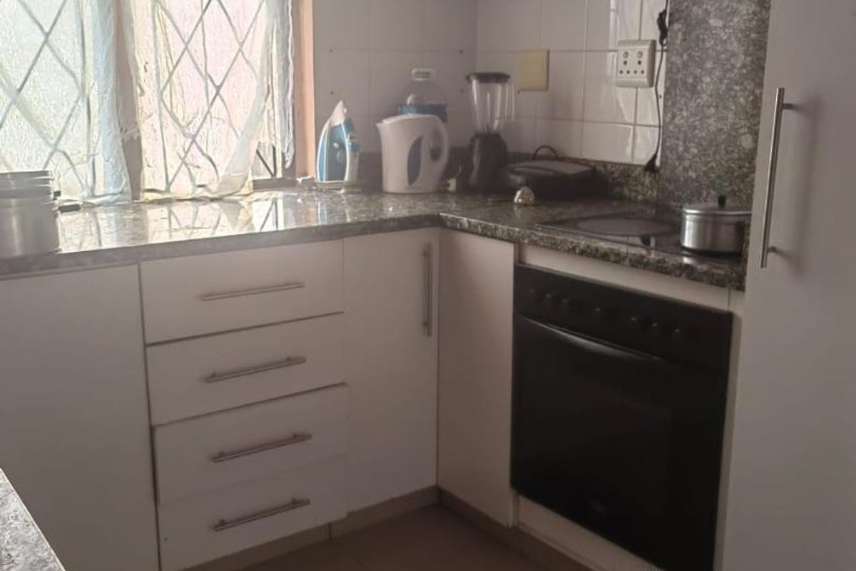 Compact kitchen featuring white cabinetry, laminate countertops, built-in oven, extractor fan, and tiled flooring.