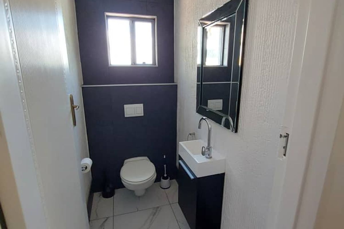 A modern guest bathroom featuring a wall-mounted toilet, a sleek vanity with a basin, and contemporary dark blue tiled accent wall.