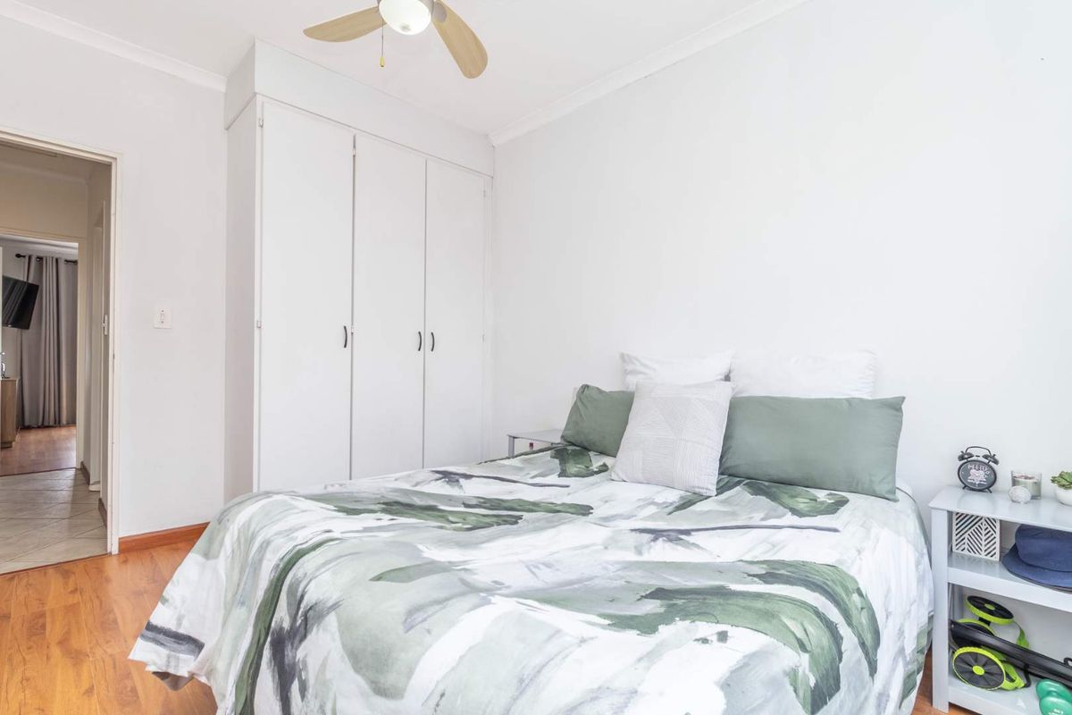 A bright bedroom featuring laminate flooring, built-in cupboards for storage, and a ceiling fan, with a view into the adjacent hallway.
