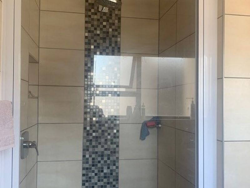 A modern shower enclosure featuring neutral wall tiles with a decorative mosaic feature strip and a built-in niche for storage.