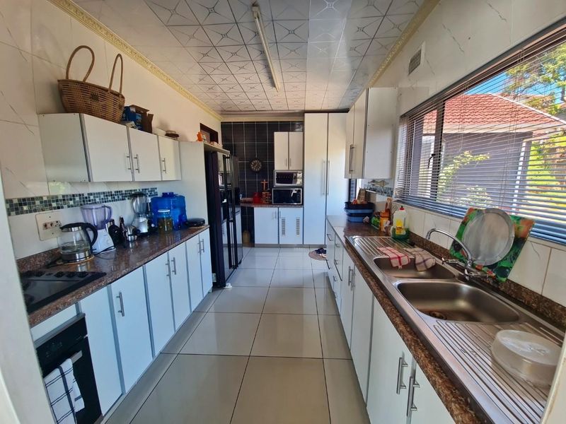 A functional galley-style kitchen featuring white cabinetry, granite countertops, a double basin sink, and tiled finishes throughout.
