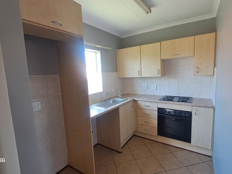 A functional kitchen featuring light wood cabinetry, laminate countertops, a built-in oven with electric hob, and tiled flooring.