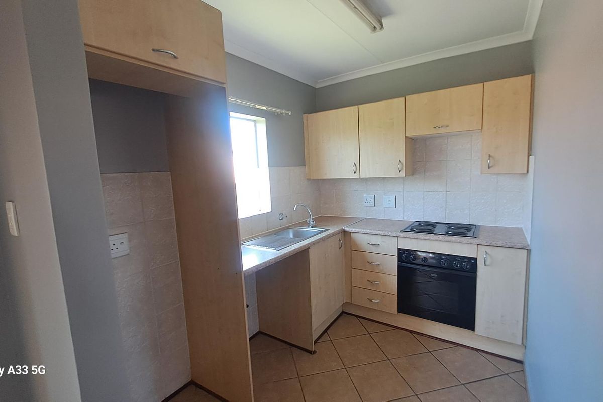 A functional kitchen featuring light wood cabinetry, laminate countertops, a built-in oven with electric hob, and tiled flooring.