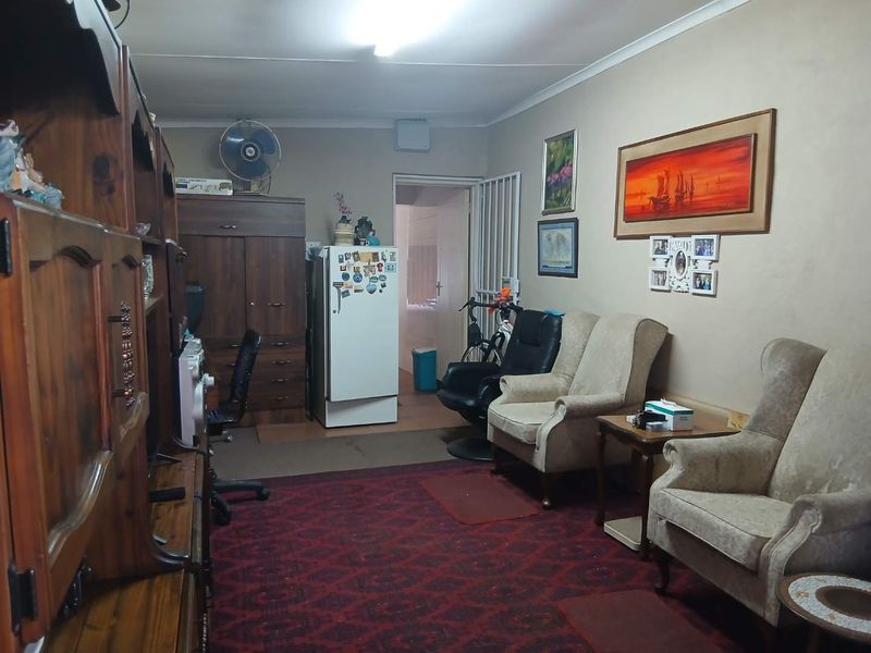 A living room area featuring neutral wall finishes, coved cornicing, and access to an adjacent room through a security gate.