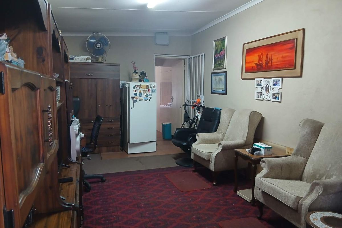 A living room area featuring neutral wall finishes, coved cornicing, and access to an adjacent room through a security gate.