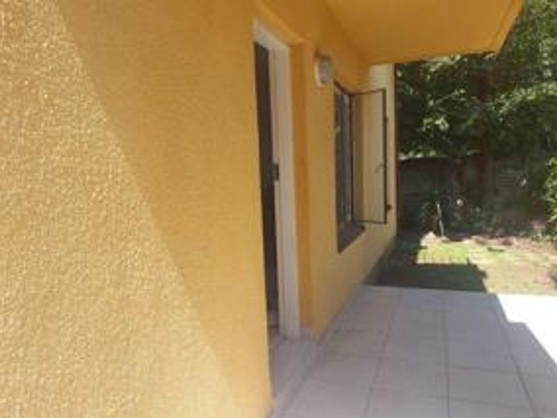 A covered patio area featuring tiled flooring, exterior wall lighting, and access to the garden space.