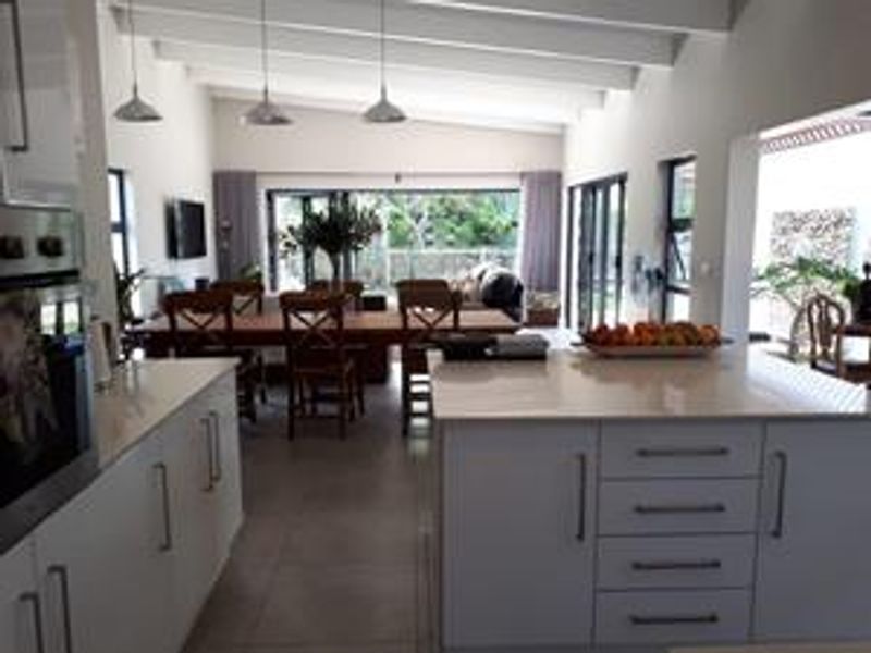 Spacious open-plan living area featuring a modern kitchen with a central island, exposed ceiling beams, and large sliding doors leading to the outdoor space.