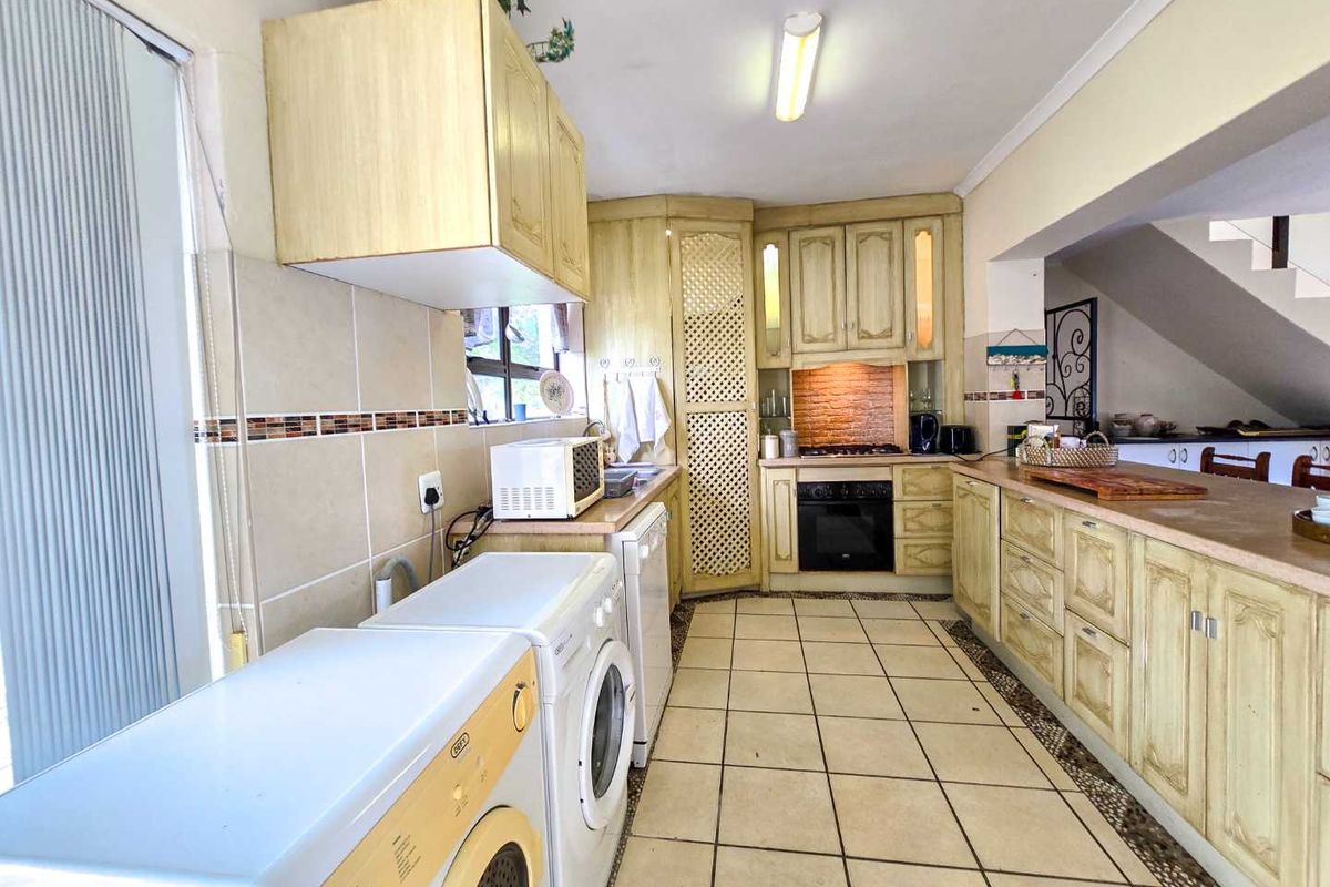 A functional kitchen featuring traditional cabinetry, built-in oven and hob, tiled flooring, and integrated laundry appliance space.