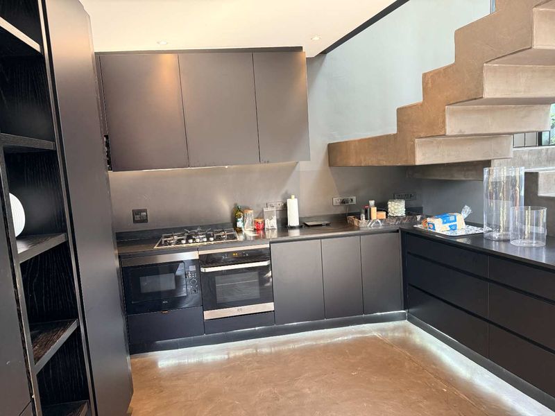 Modern kitchen featuring sleek dark cabinetry, integrated appliances, gas hob, and a striking concrete staircase, creating a contemporary and functional culinary space.