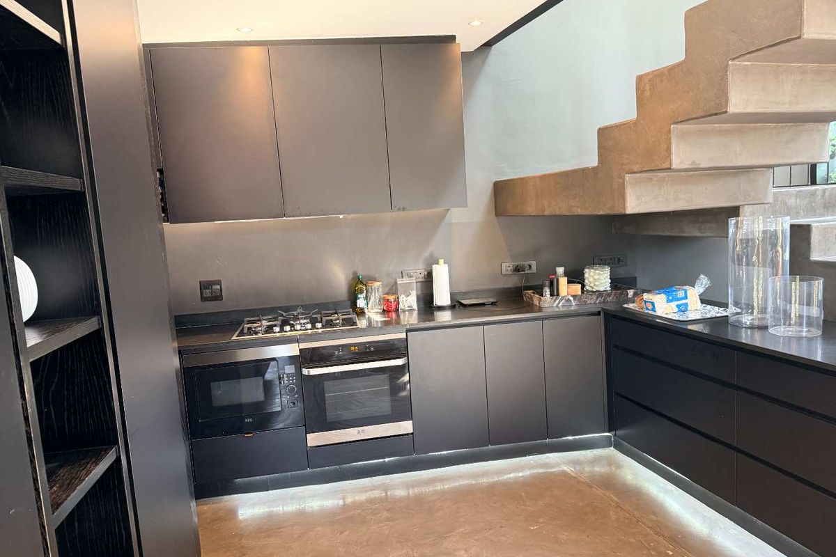 Modern kitchen featuring sleek dark cabinetry, integrated appliances, gas hob, and a striking concrete staircase, creating a contemporary and functional culinary space.