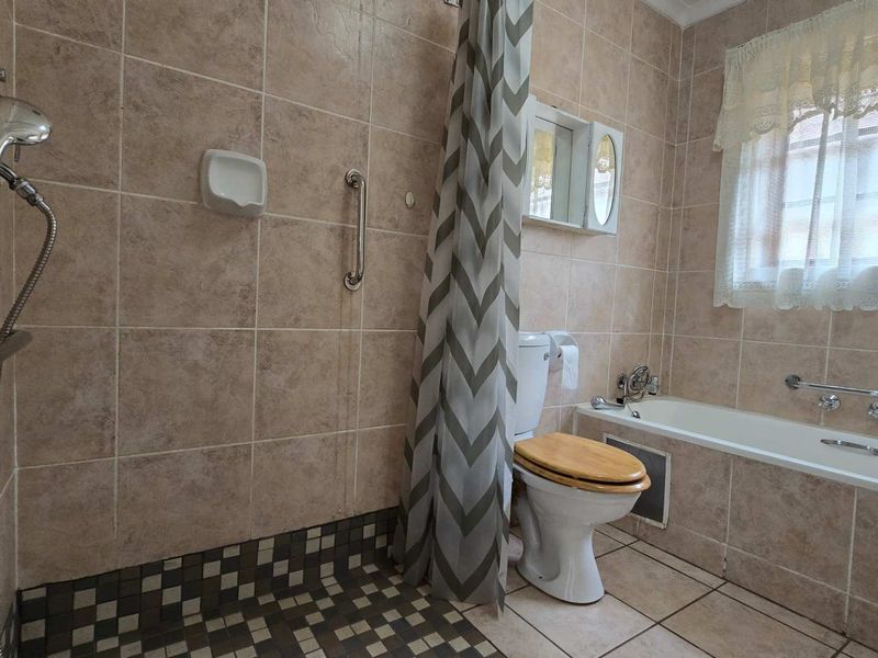 A functional bathroom featuring a walk-in shower with grab rails, a bathtub, and neutral wall tiling, suitable for retirement living requirements.