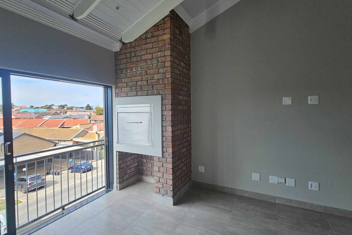 A bright living area featuring a built-in brick fireplace, tiled flooring, vaulted ceilings, and sliding glass doors opening onto a balcony with neighborhood views.