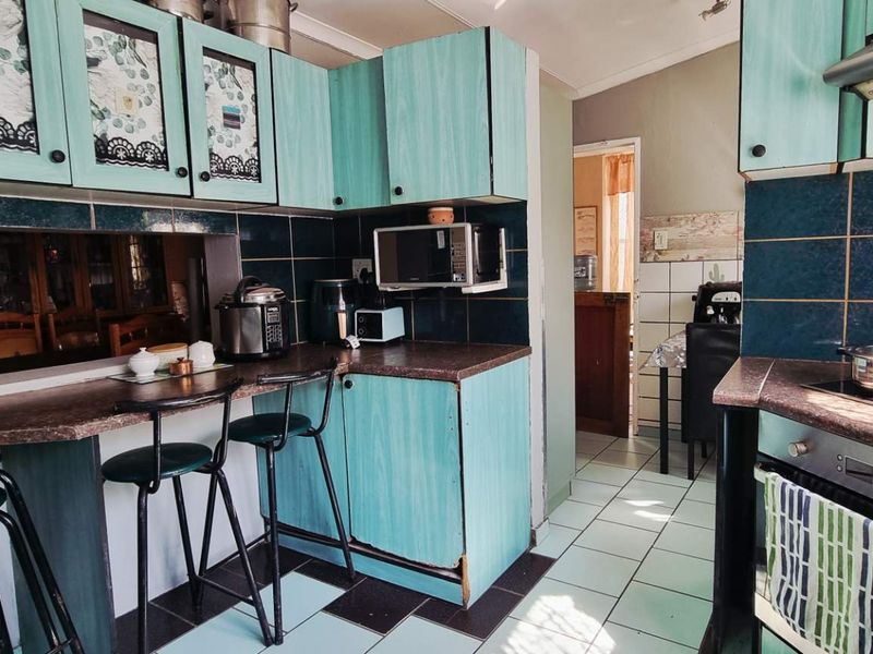 A dated kitchen featuring teal cabinetry, dark tiled backsplash, built-in oven, and a breakfast bar area with tiled flooring.