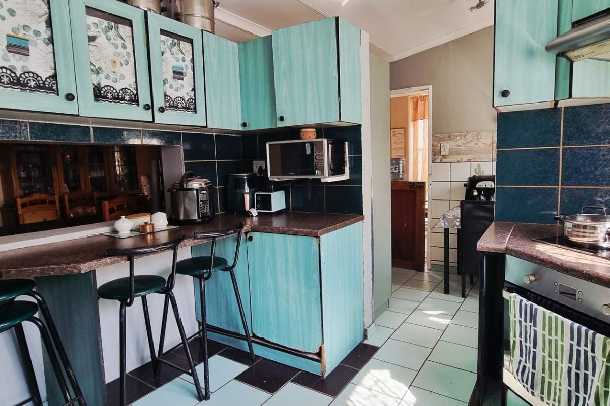 A dated kitchen featuring teal cabinetry, dark tiled backsplash, built-in oven, and a breakfast bar area with tiled flooring.