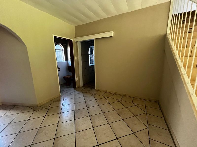 An empty hallway featuring tiled flooring, a staircase with a balustrade, and access to adjacent rooms through an archway and sliding door.