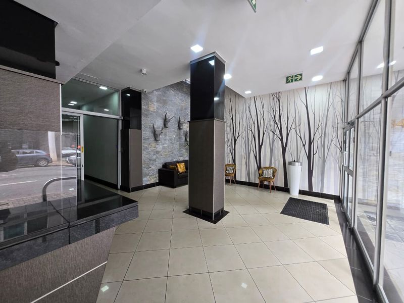 Modern apartment building entrance lobby featuring tiled flooring, a stone feature wall, and a glass facade providing natural light.