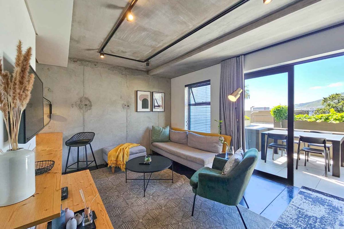 Modern open-plan living area featuring exposed concrete walls and ceiling, track lighting, and large sliding glass doors leading to a private balcony.