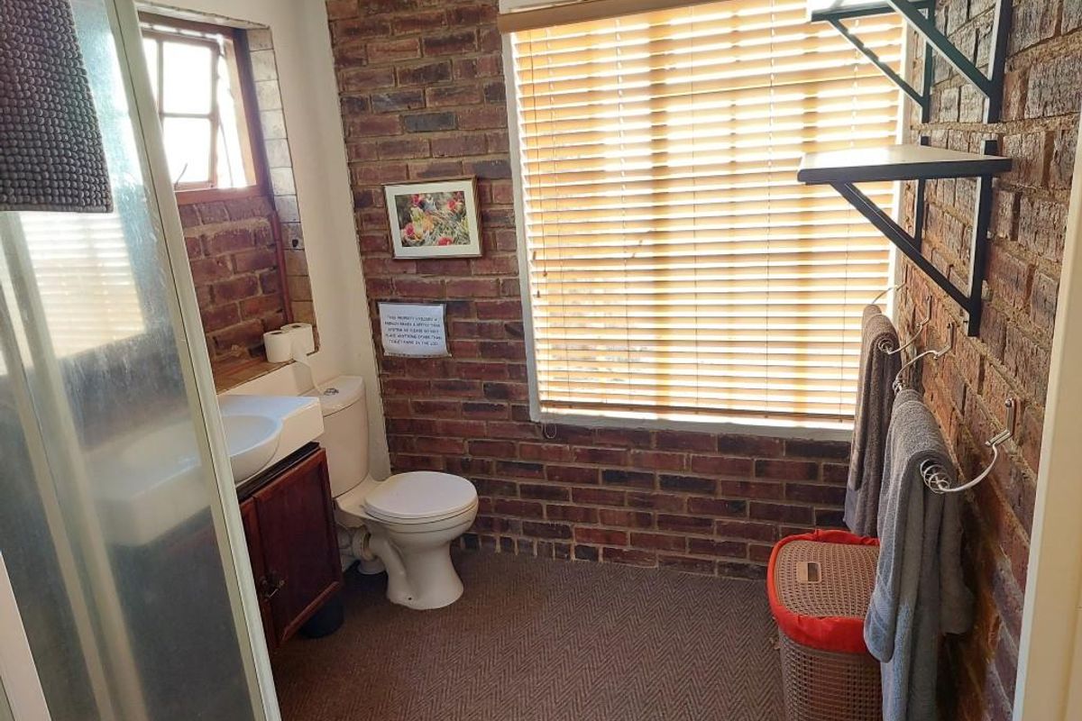 A functional bathroom featuring exposed brick walls, a shower enclosure, a vanity basin, and a toilet, with natural light provided by a window.
