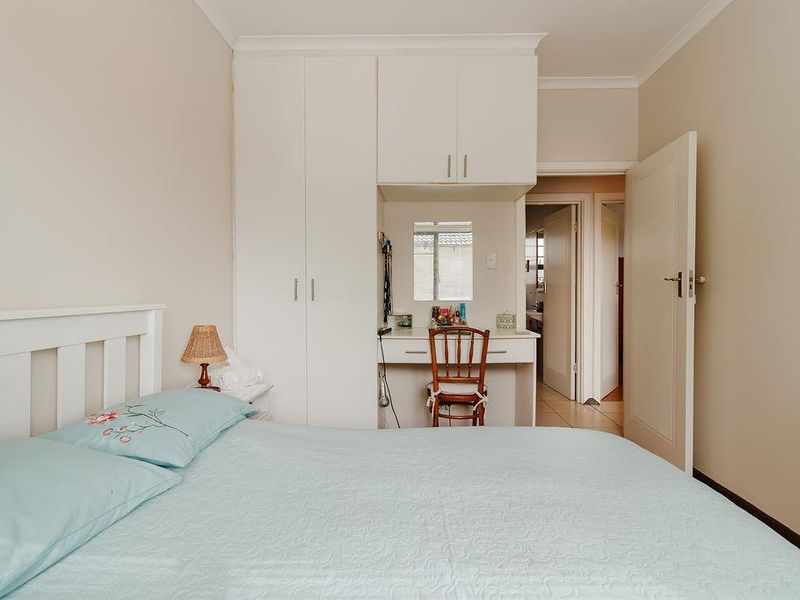 A bedroom featuring built-in cabinetry with an integrated vanity area, neutral wall finishes, and access to an adjoining hallway.