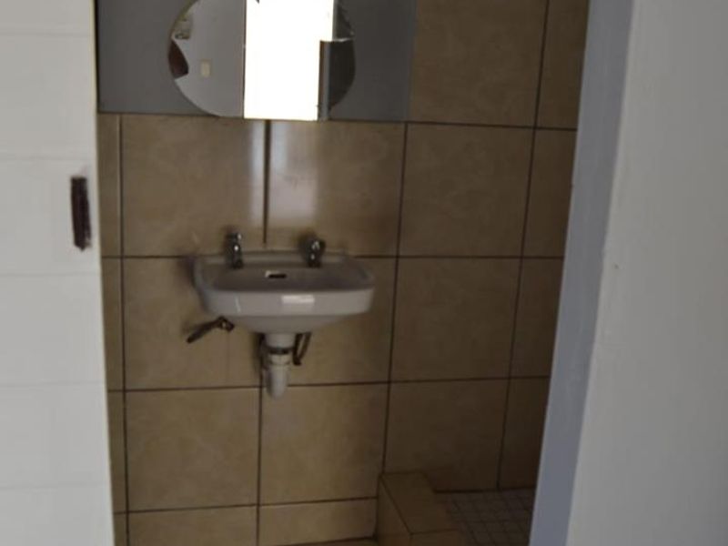 A compact bathroom featuring a wall-mounted basin and tiled finishes, currently in need of modernization and cosmetic updates.
