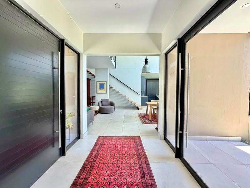 Spacious modern entrance hall featuring a large pivot door, tiled flooring, and a striking floating staircase leading to the open-plan living area.